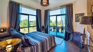 A bedroom with a large bed, two windows with curtains, a hanging light fixture, and a view of greenery outside. - The Paris Suite cottage - gorgeous views on 7 acres Mapua seaside village Nelson (Upper Moutere)