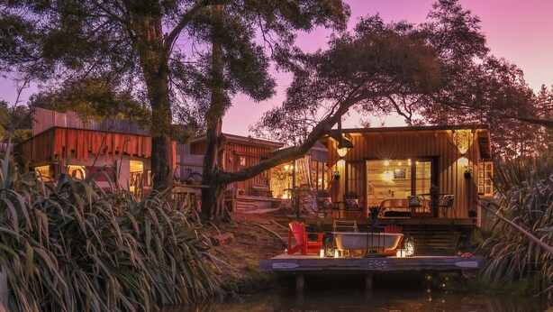 A rustic cabin with a dock extending into a calm body of water, surrounded by lush vegetation. - The Paris Suite cottage - gorgeous views on 7 acres Mapua seaside village Nelson (Upper Moutere)