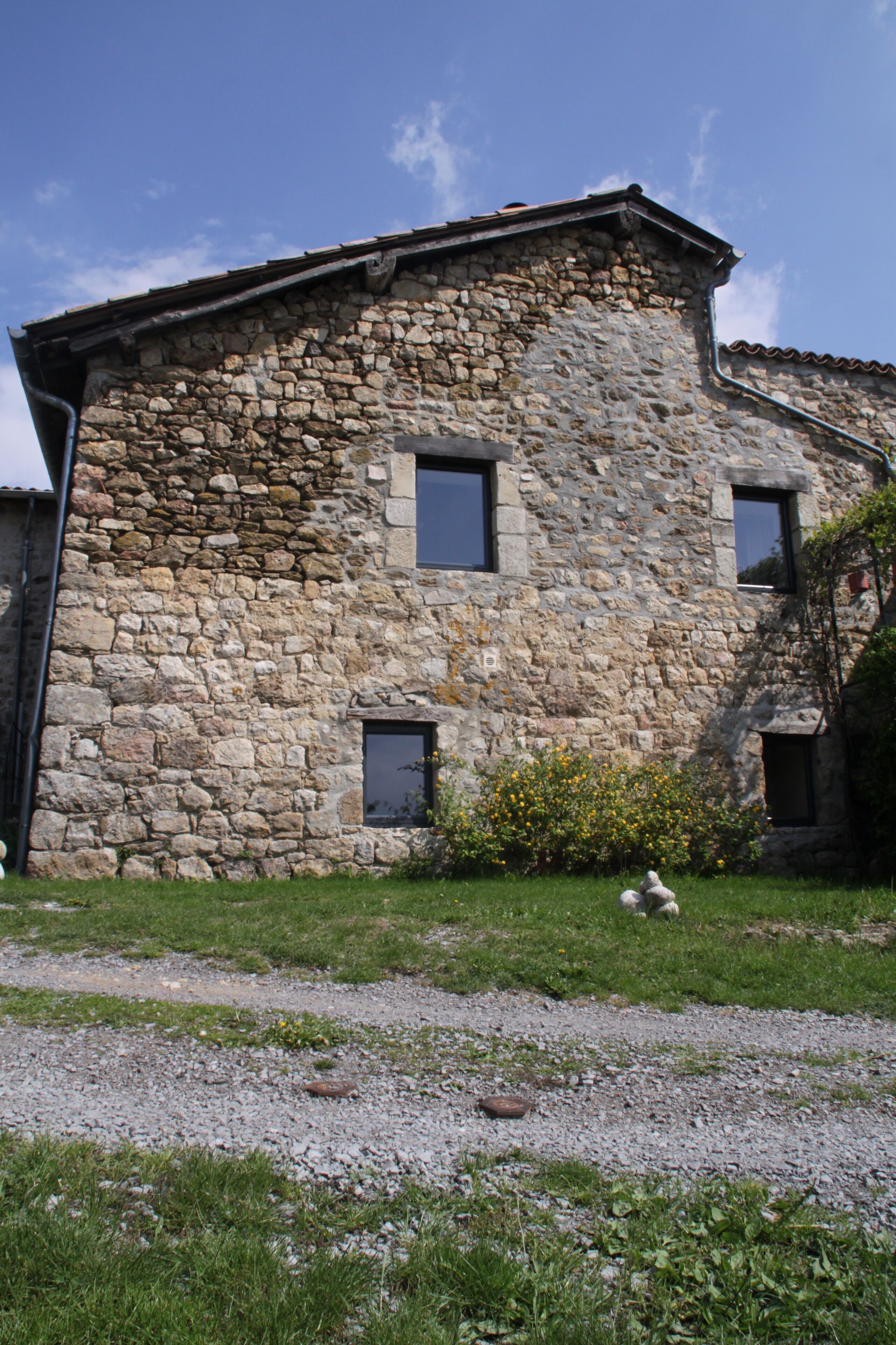 A stone building with three windows and a small garden area.