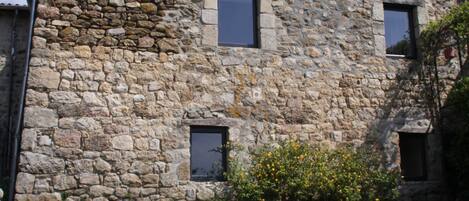 Un edificio de piedra con tres ventanas y un pequeño jardín.
