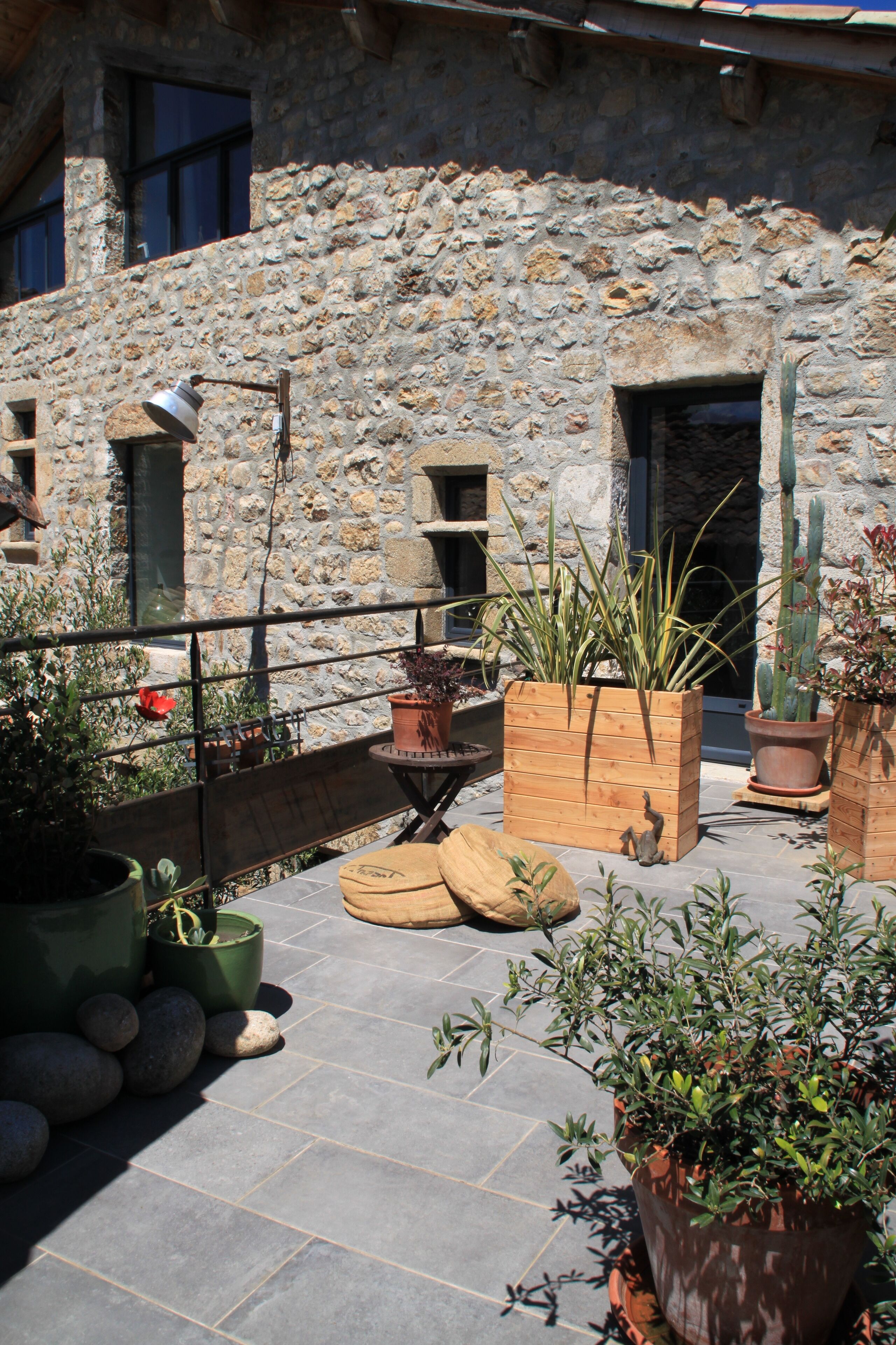 A stone building with a rooftop garden featuring potted plants and a wooden bench.