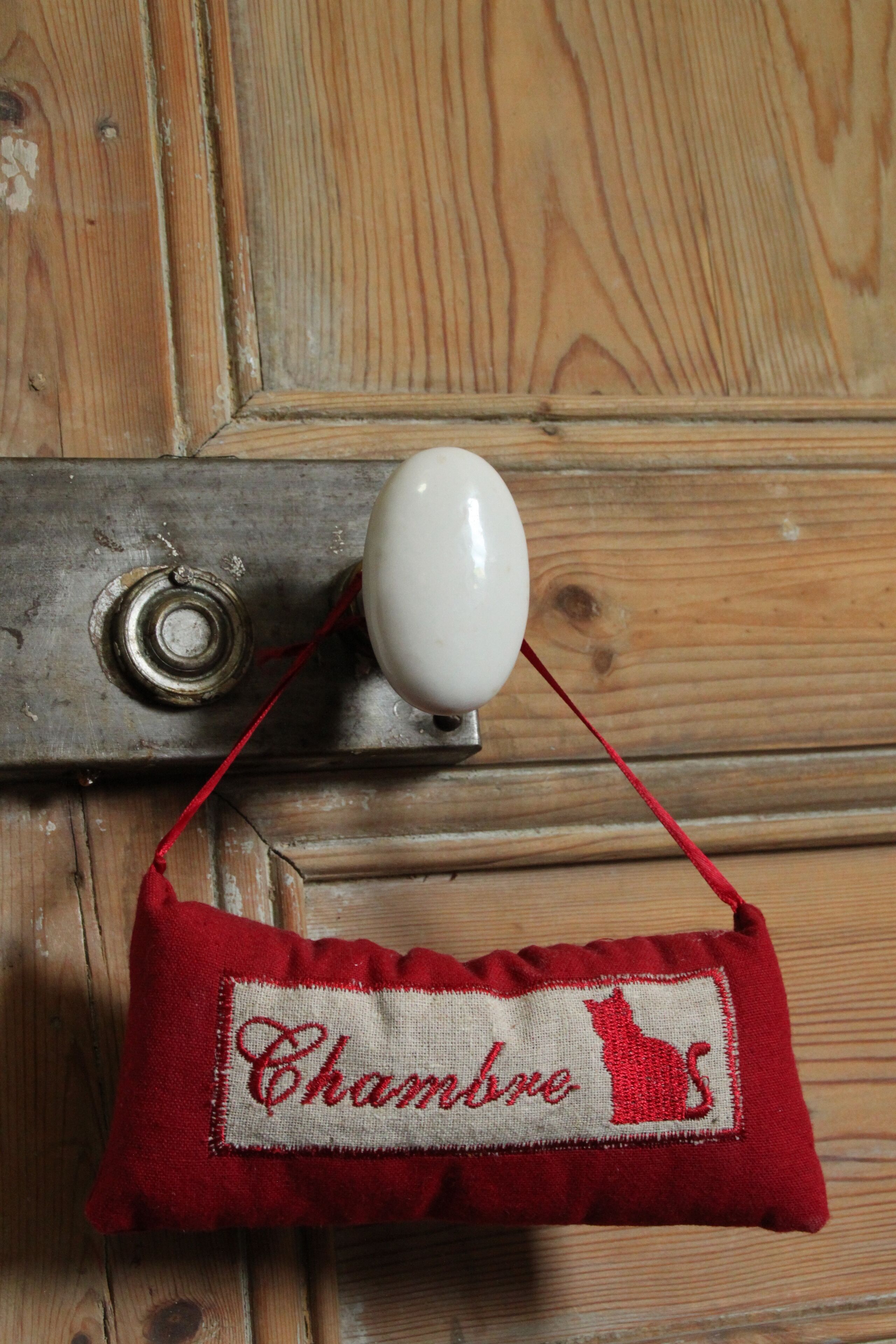 A wooden door with a brass doorknob and a small white object hanging on a red string.