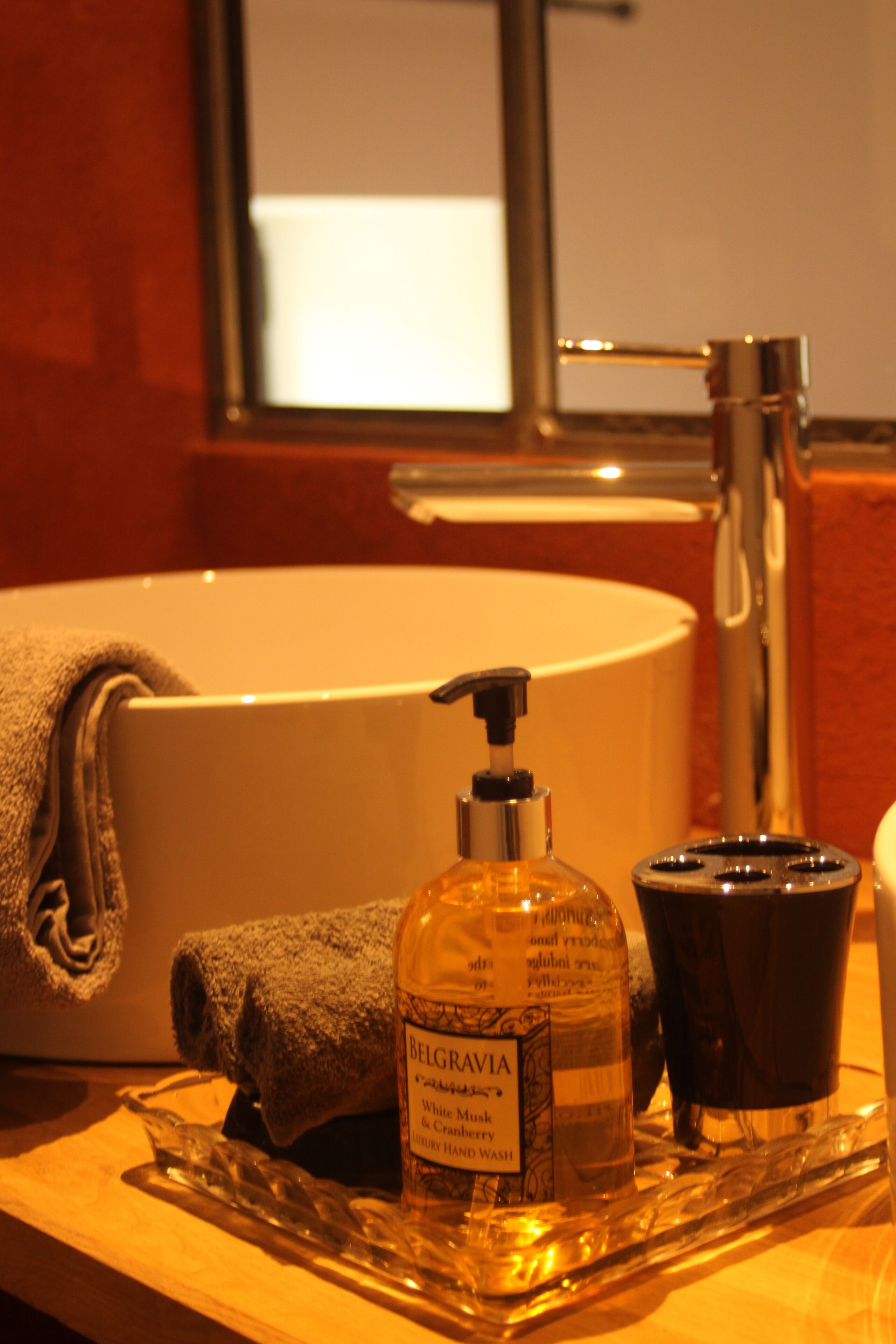 A bathroom sink with a towel, a bottle of hand wash, and a black soap dispenser on a tray.
