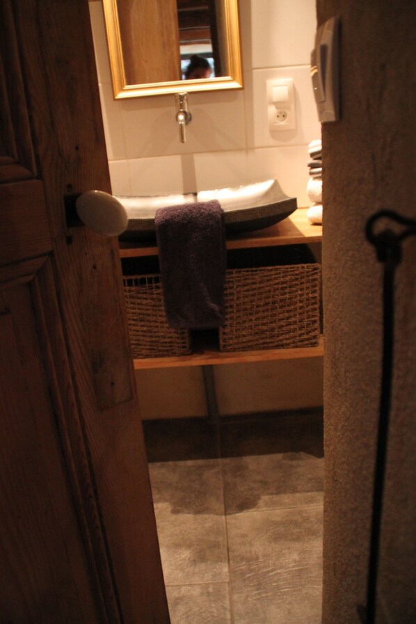 A bathroom with a wooden door, a mirror, a sink, and a towel hanging on a rack. - La Demeure Des Maitres (Chirols)