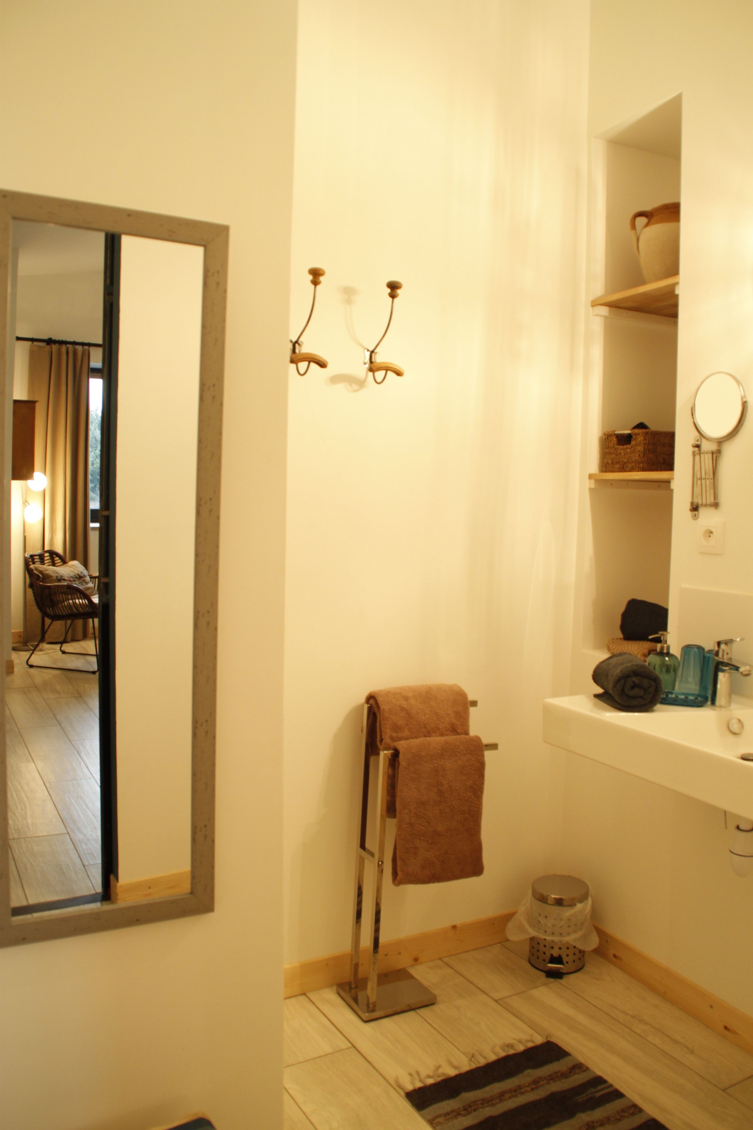 Een badkamer met een spiegel, handdoekhouder, wastafel en planken met toiletartikelen.