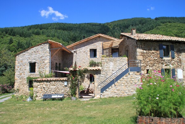 A stone house with a staircase leading to the upper floor, surrounded by greenery and hills. - La Demeure Des Maitres (Chirols)