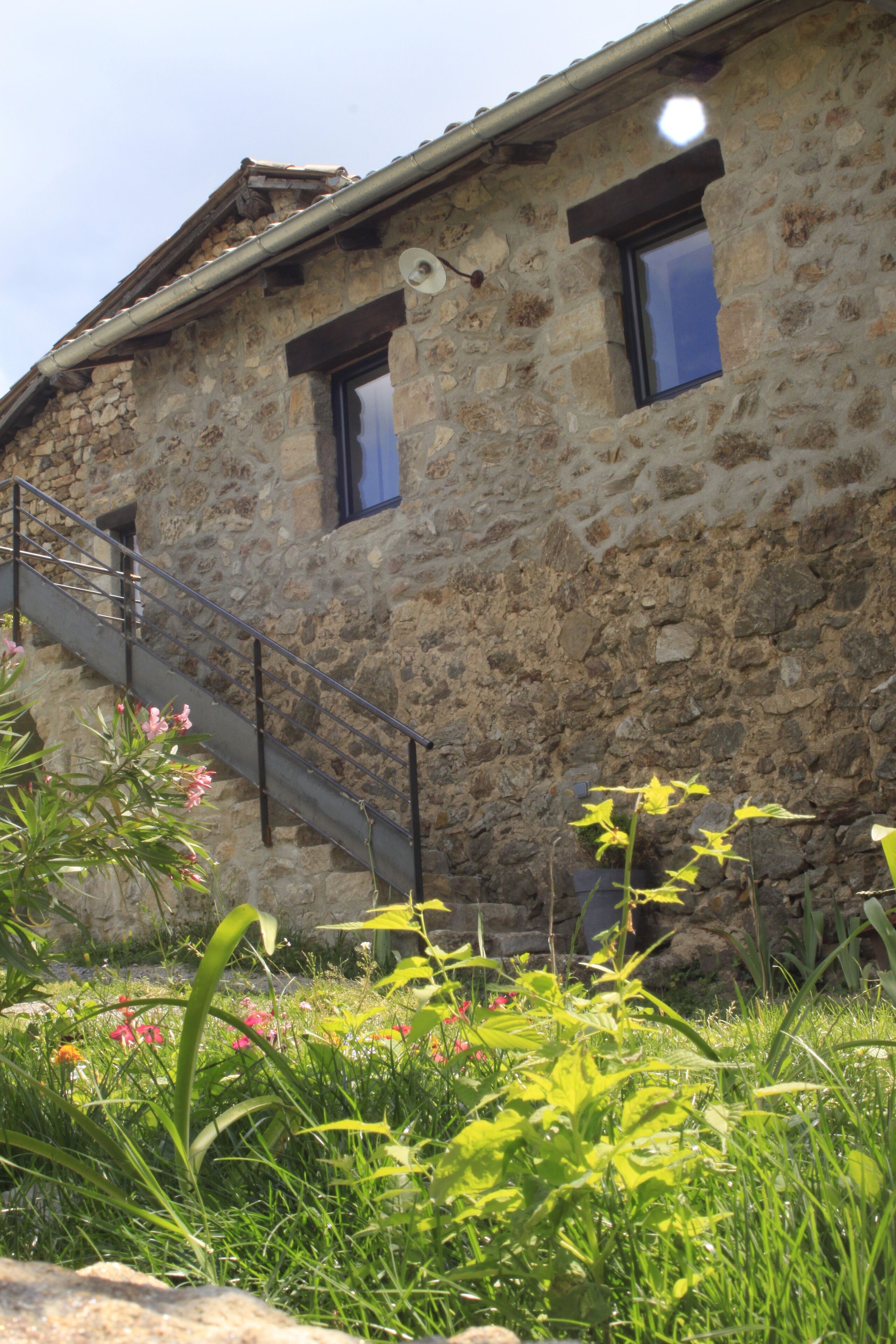 Un edificio de piedra con una escalera que lleva a una ventana, rodeado de follaje y flores.
