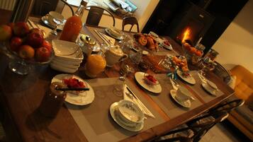 A dining table set with plates, bowls, and various food items, surrounded by chairs and a fireplace in the background.