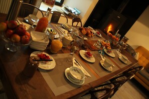 A dining table set with plates, bowls, and various food items, surrounded by chairs and a fireplace in the background. - La Demeure Des Maitres (Chirols)