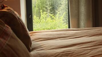Un dormitorio con cama, lámpara y ventana con vistas a un bosque.