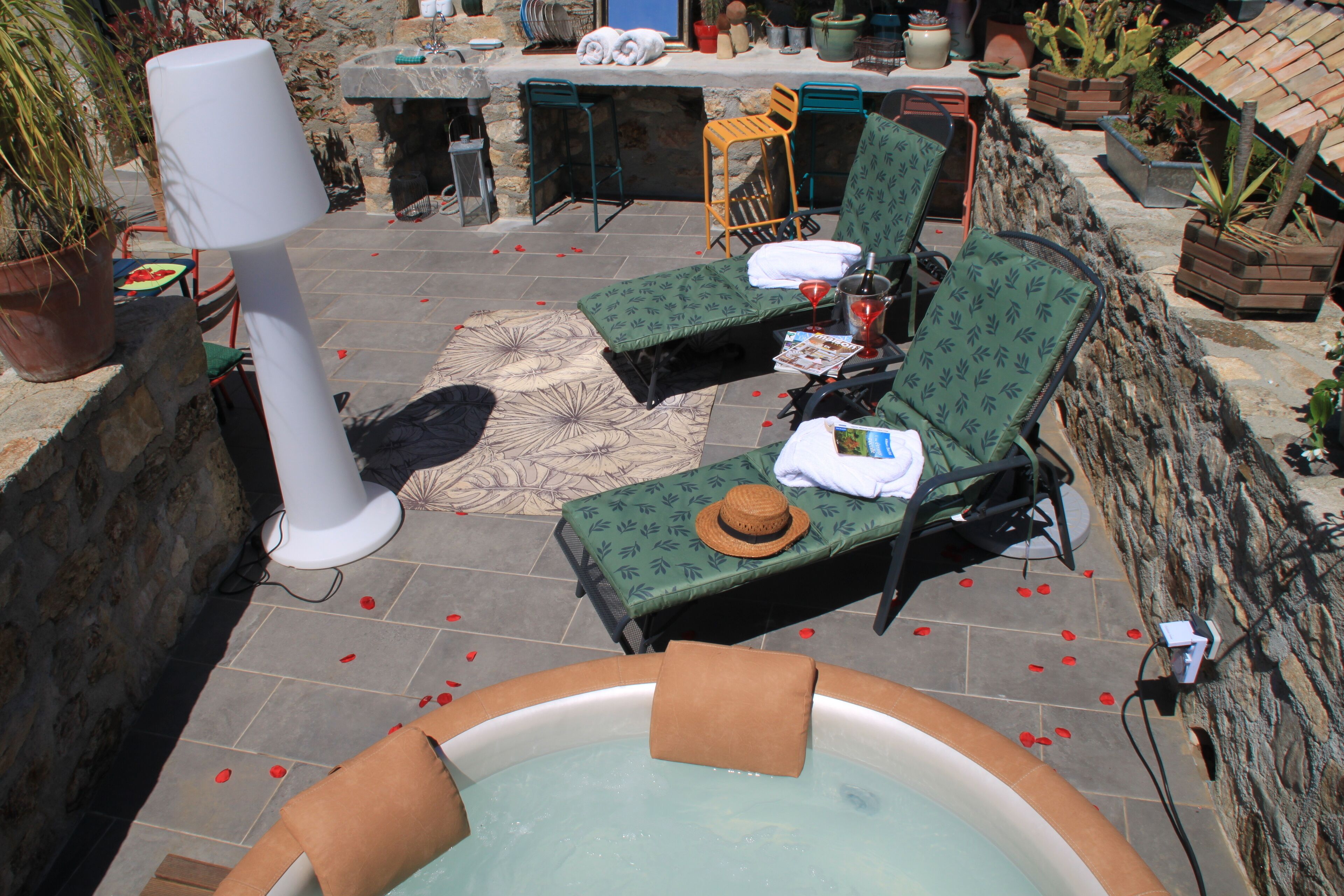 A hot tub surrounded by lounge chairs and a table with a hat on it.