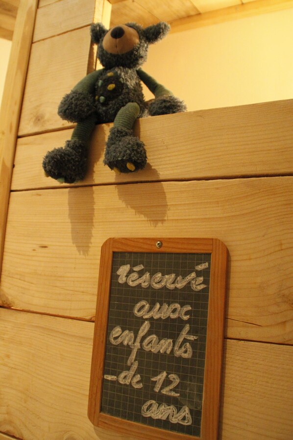 Pared de madera con un osito de peluche y un cartel de pizarra que dice 'reservado con niños menores de 12 años'.