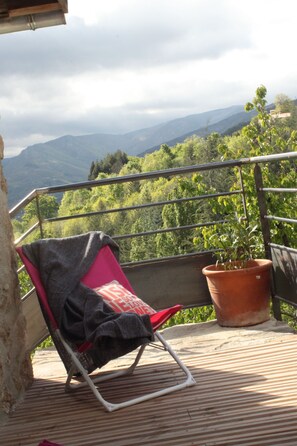 A balcony with a red chair, a potted plant, and a view of green hills and mountains. - La Demeure Des Maitres (Chirols)