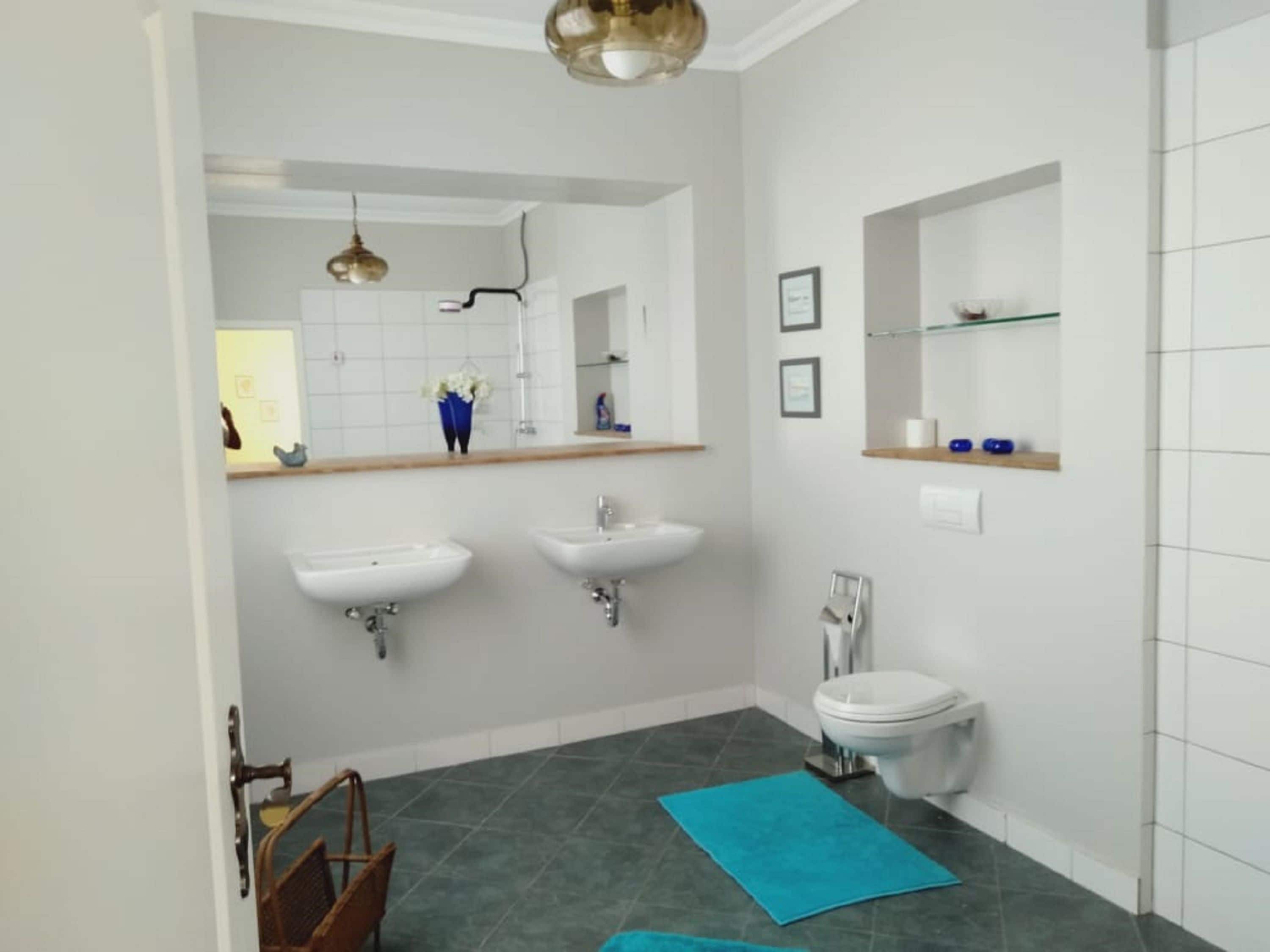 Een badkamer met twee wasbakken, een toilet, een spiegel en een blauwe handdoek op de vloer.