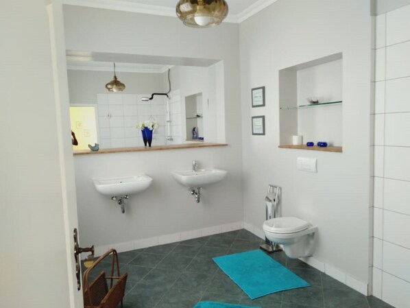 A bathroom with two sinks, a toilet, a mirror, and a blue towel on the floor.