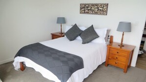 A neatly made bed with a quilted blanket, two bedside tables with lamps, and a wall art piece above the bed. - SPECTACULAR SEA VIEWS!! New Modern Apartment overlooking Bay.  (Oneroa)