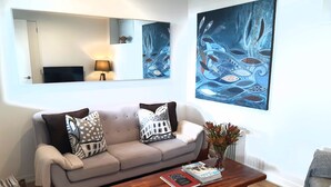 A living room with a sofa, coffee table, and two paintings. - SPECTACULAR SEA VIEWS!! New Modern Apartment overlooking Bay.  (Oneroa)