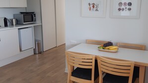 A modern kitchen with white cabinets, a microwave, and a small refrigerator. There is a dining table with two chairs and a fruit basket on it. - SPECTACULAR SEA VIEWS!! New Modern Apartment overlooking Bay.  (Oneroa)