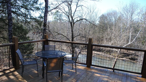 A wooden deck with a round table and chairs, overlooking a river and surrounded by trees. - Beautiful secluded cottage with gated privacy. (Smithville)