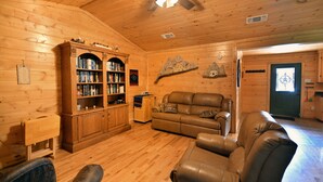 A log cabin interior with a leather sofa, wooden bookshelves, and a ceiling fan. - Beautiful secluded cottage with gated privacy. (Smithville)