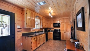 A wooden cabin kitchen with a central island, built-in microwave, and black stove. - Beautiful secluded cottage with gated privacy. (Smithville)