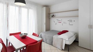 Ein kompakter Raum mit einem Bett, einem Esstisch mit Stühlen und einer Wand mit mehrsprachigen Willkommensschildern.