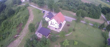 An aerial view of a house with a red roof, surrounded by green fields and trees.