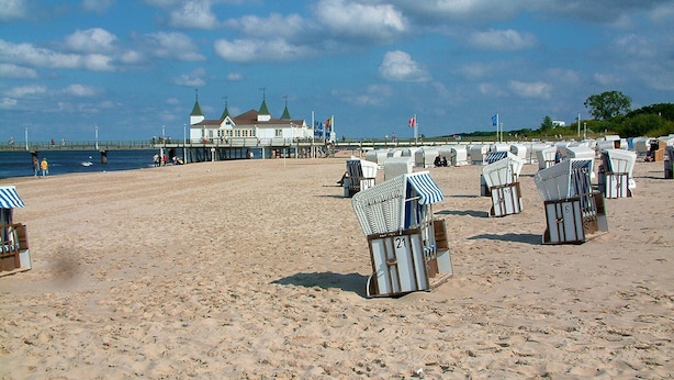 Une plage avec des rangées de chaises de plage numérotées et une jetée sur laquelle se trouve un bâtiment en arrière-plan.
