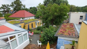 Une cour avec un toit recouvert de tuiles rouges, un bâtiment jaune et un arbre.