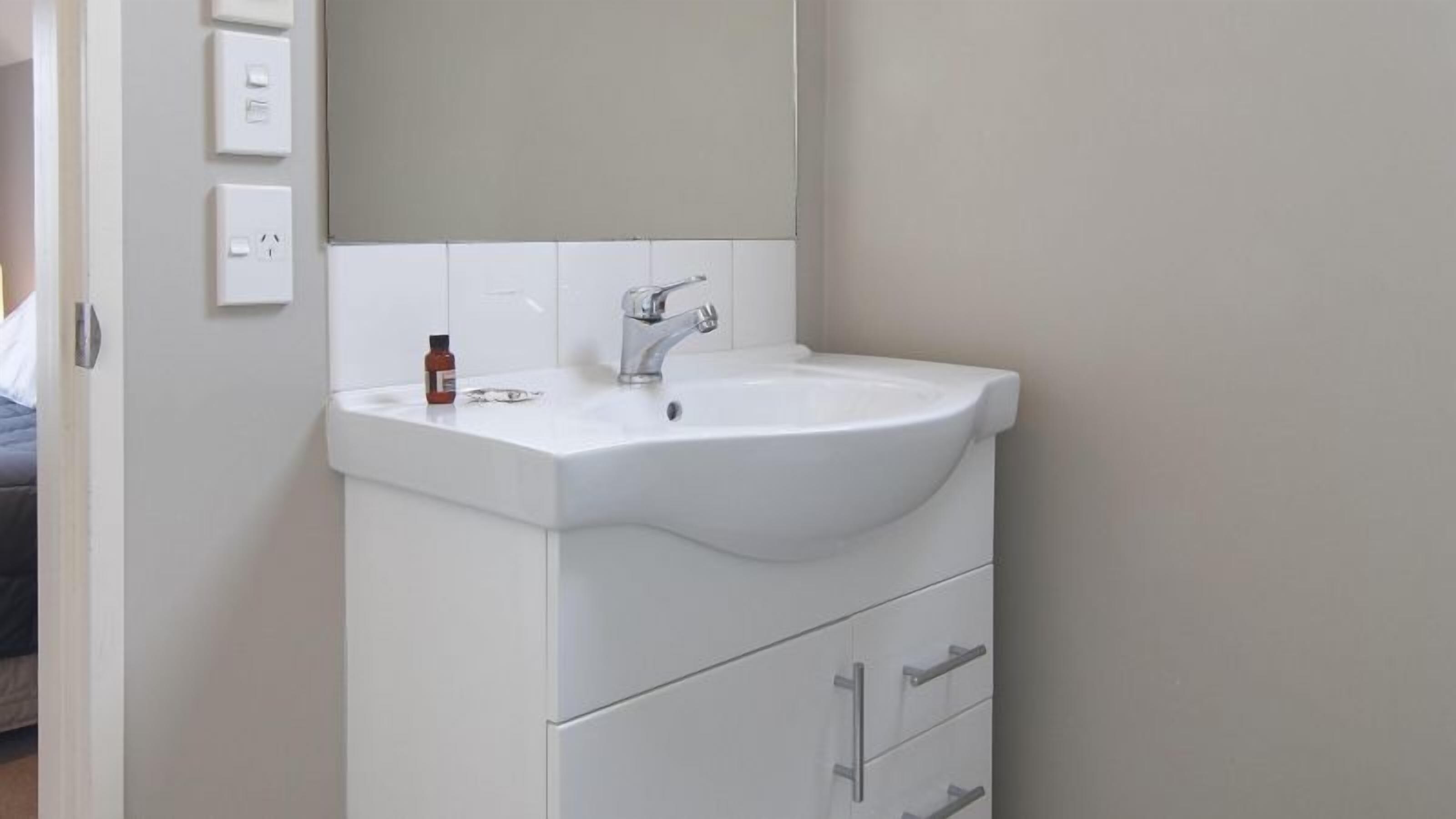 Un baño con un lavamanos blanco, un espejo y una botella de medicamentos sobre el lavamanos.