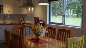 A modern kitchen with white cabinets, a wooden dining table, and a large window offering a view of a grassy area.