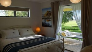 A bedroom with a bed, a nightstand, a lamp, a painting, and a view of a garden.