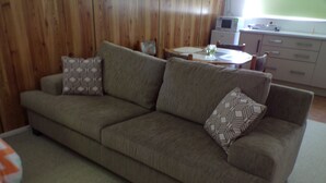 A living room with a sofa, patterned cushions, a dining table, and a kitchen area in the background.