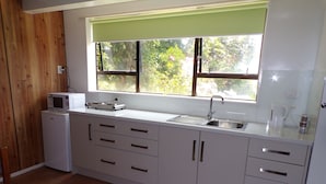 A compact kitchen with white cabinets, a built-in microwave, a sink, and a window with a green blind.