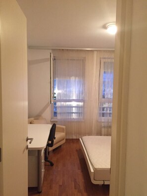 Een kamer met een bed, een bureau en een stoel. Er is een raam met gordijnen.