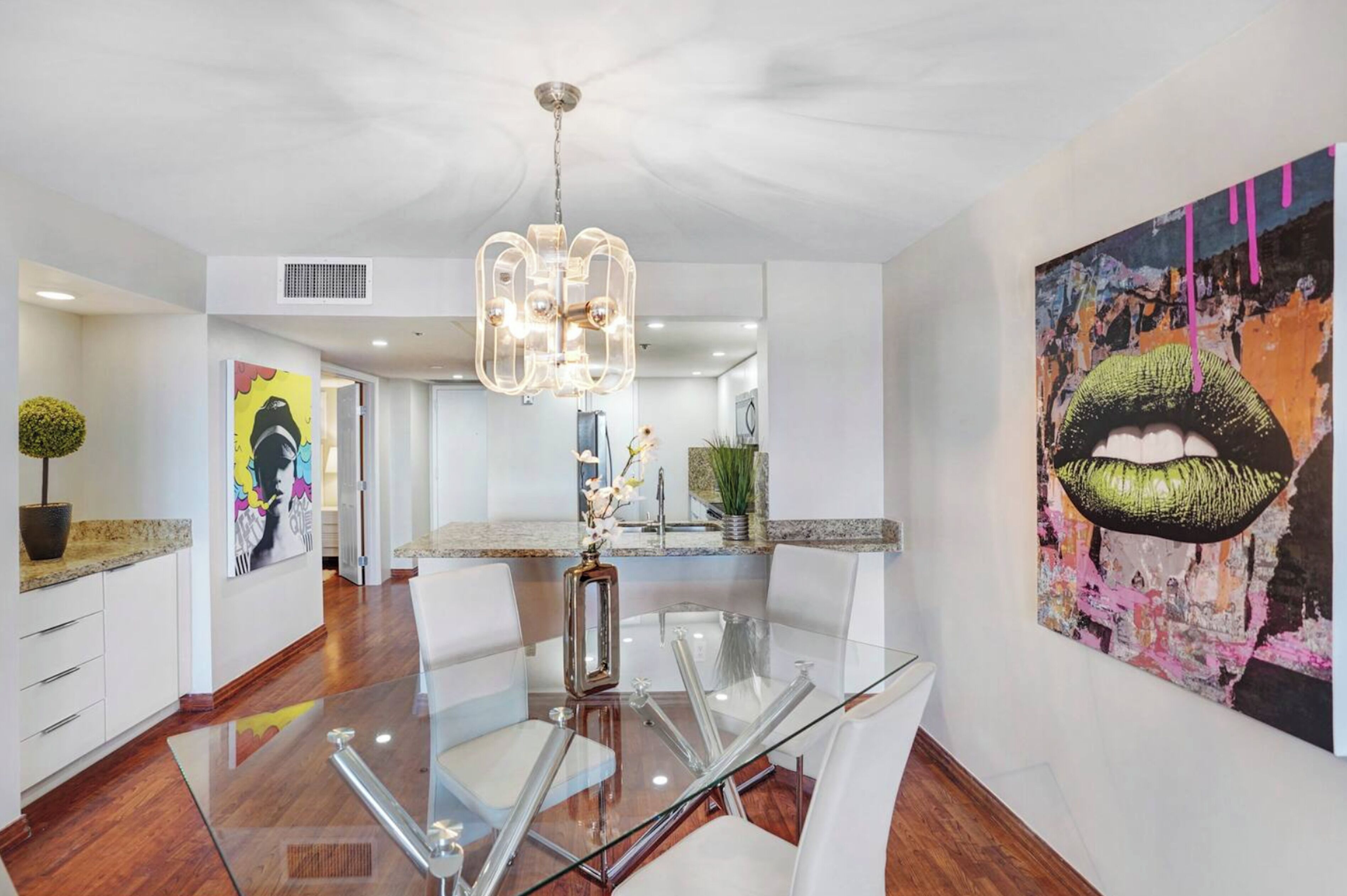 A modern kitchen with a glass dining table, white cabinetry, and a central island.