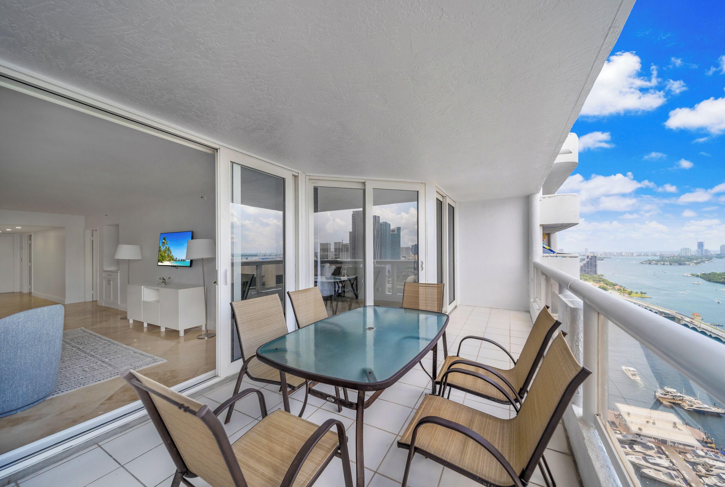 A balcony with a glass table and chairs, a TV, and a view of the city and water.