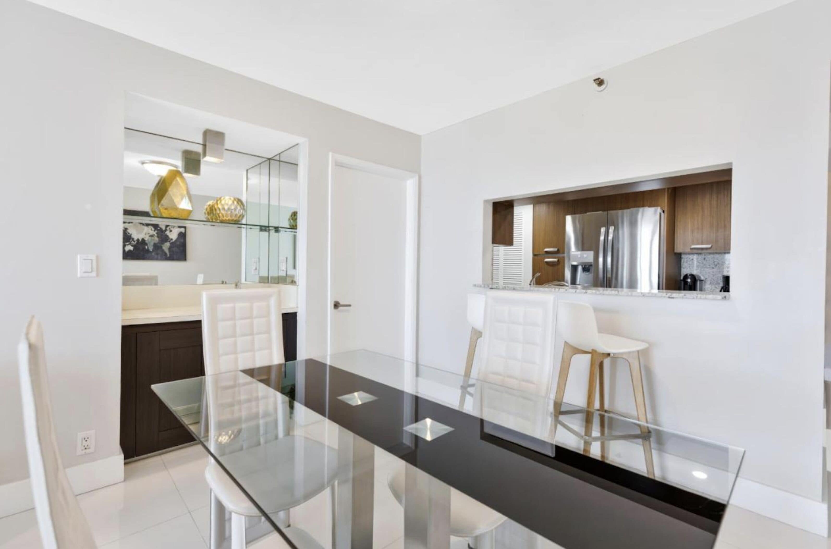 A modern kitchen with a built-in refrigerator, a countertop with a sink, and a glass dining table with chairs.