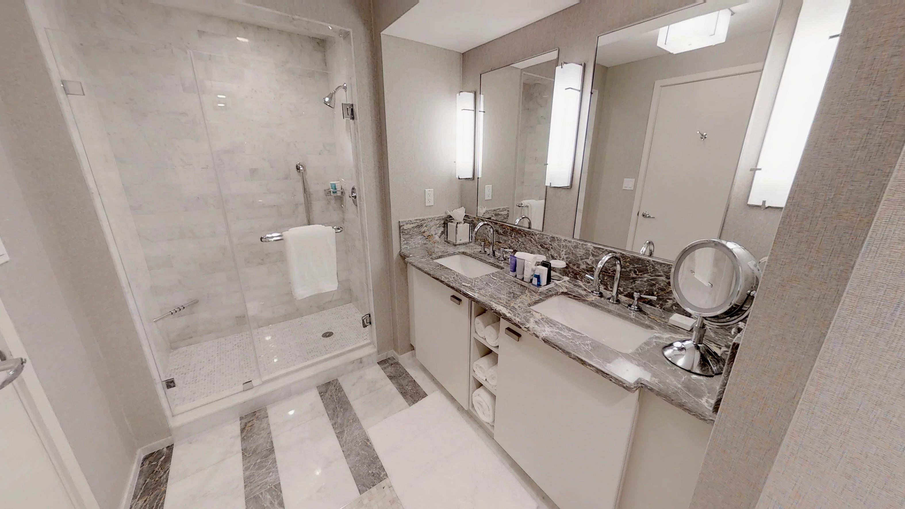 A modern bathroom with a glass-enclosed shower, a marble countertop, and a large mirror.