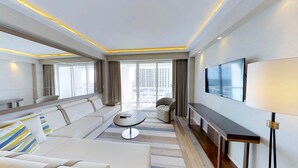 Une chambre d’hôtel moderne, dotée d’un canapé, d’une petite table ronde, d’un téléviseur fixé au mur et d’un balcon offrant une vue sur la ville.