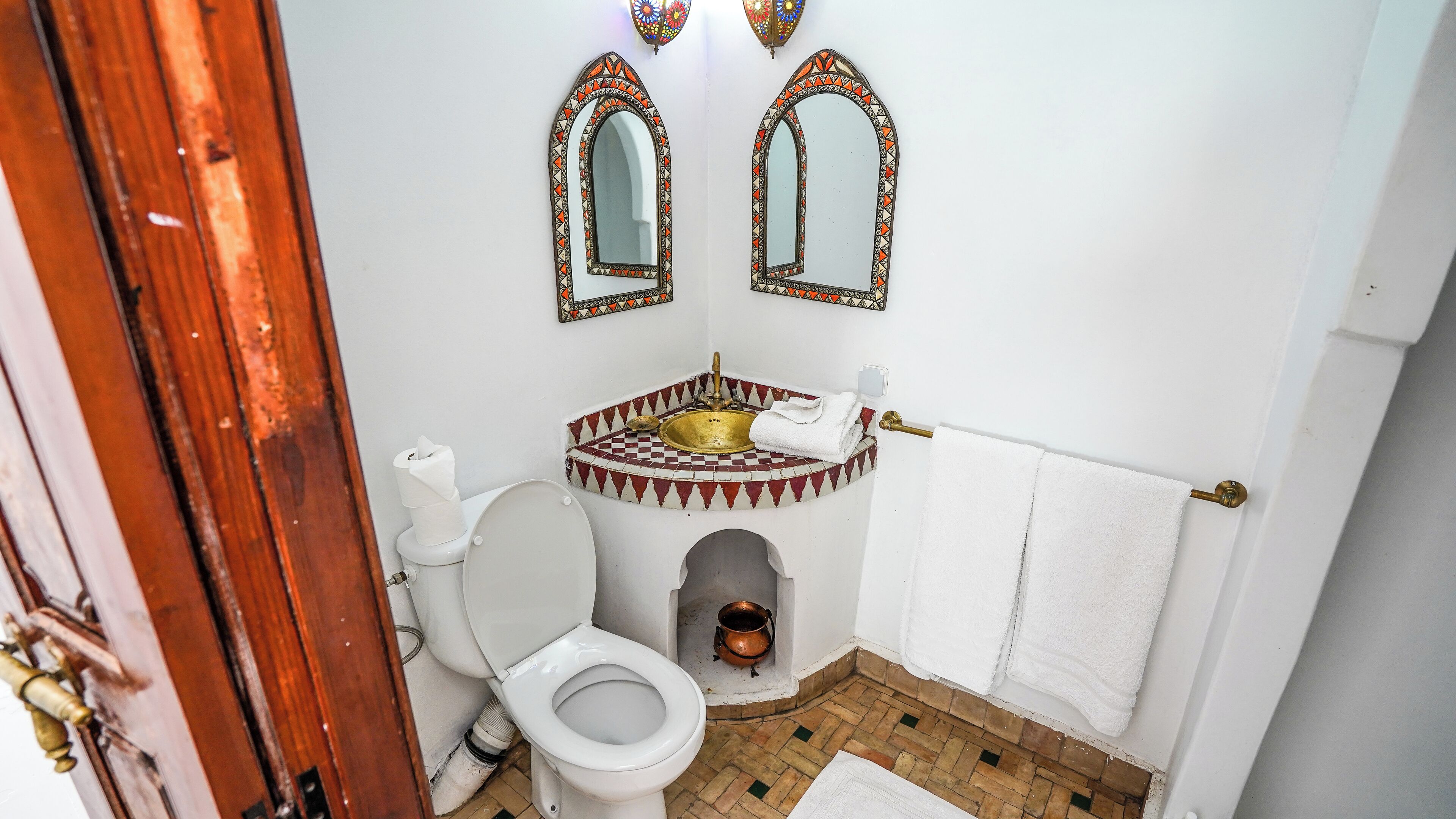 A bathroom with a white toilet, a sink with a copper basin, and a mirror with a decorative frame.