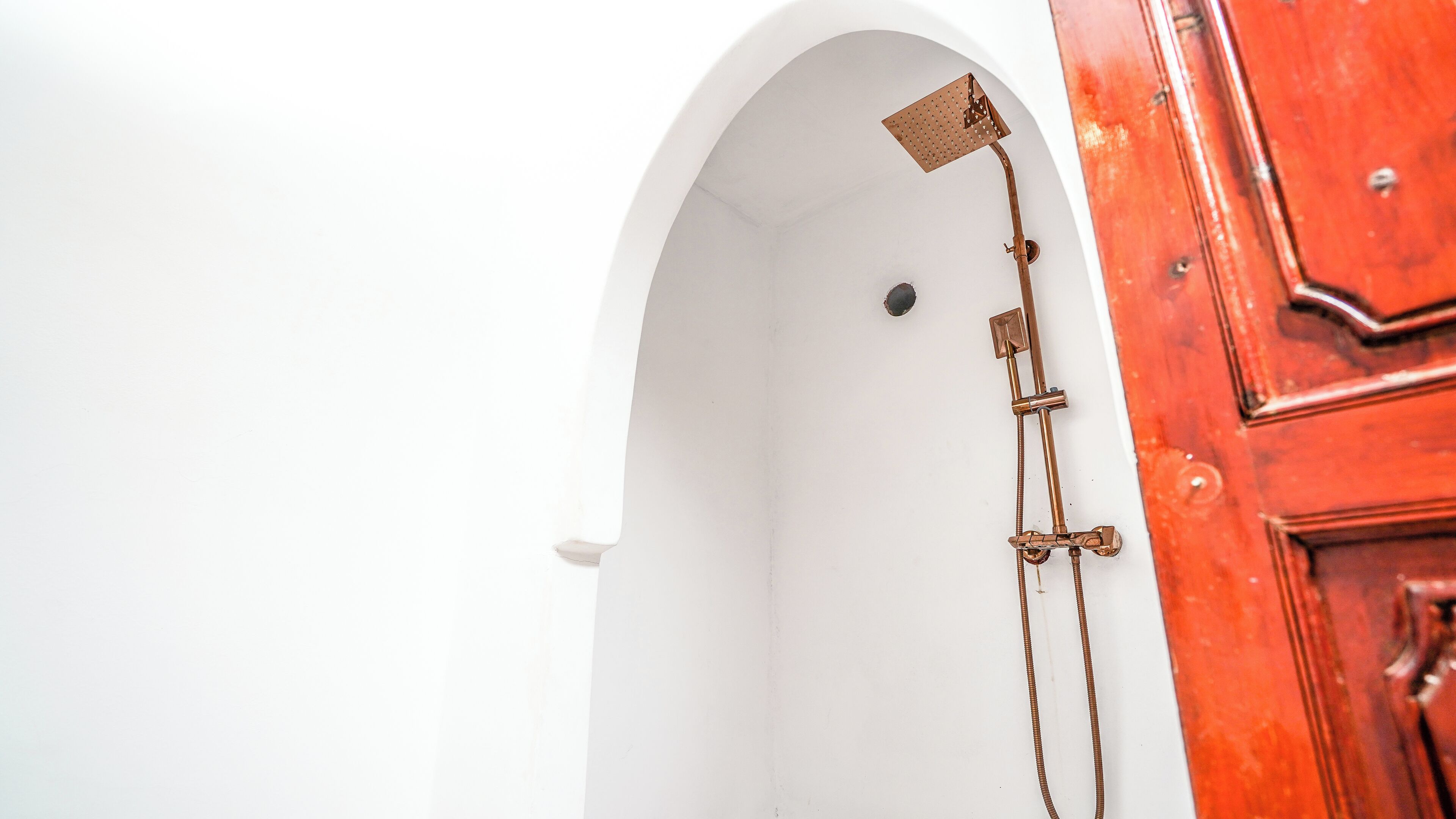 A white arched doorway leading to a shower area with a showerhead and hose.
