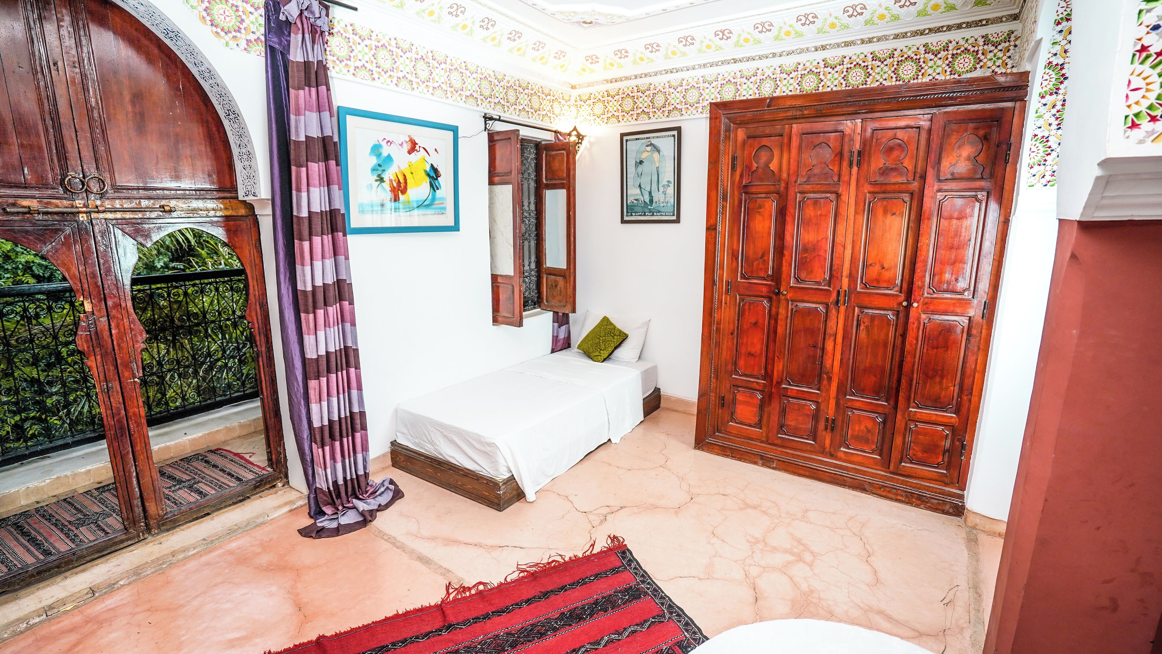 Une chambre à coucher avec un lit, une armoire en bois, une fenêtre avec un rideau et un mur orné d’un tableau encadré.