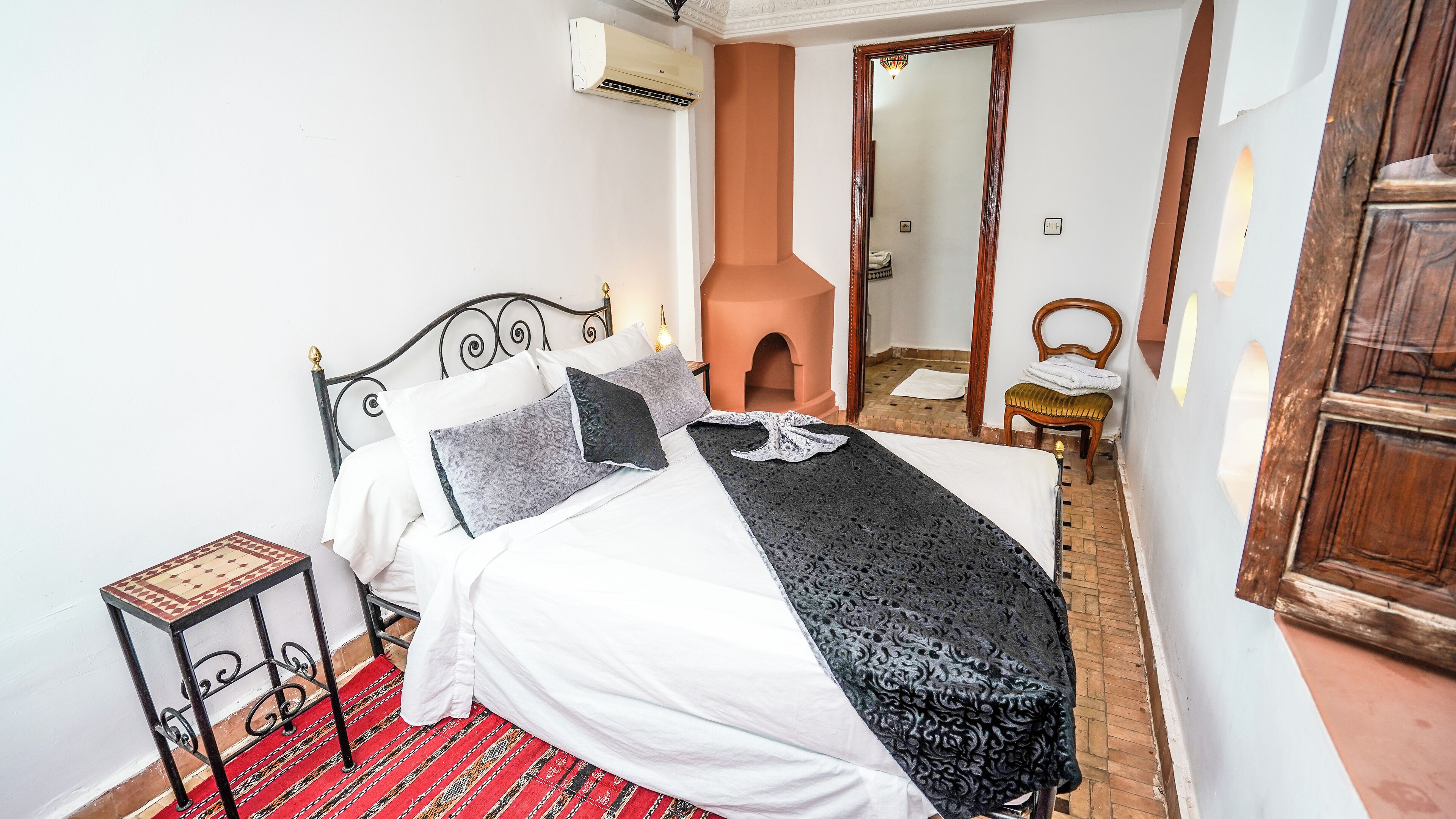 A neatly made bed with a patterned blanket, a small side table, and a red patterned rug.