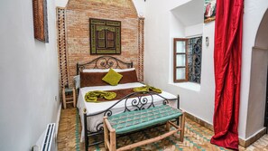 A room with a bed, a bench, a red curtain, and a brick wall.