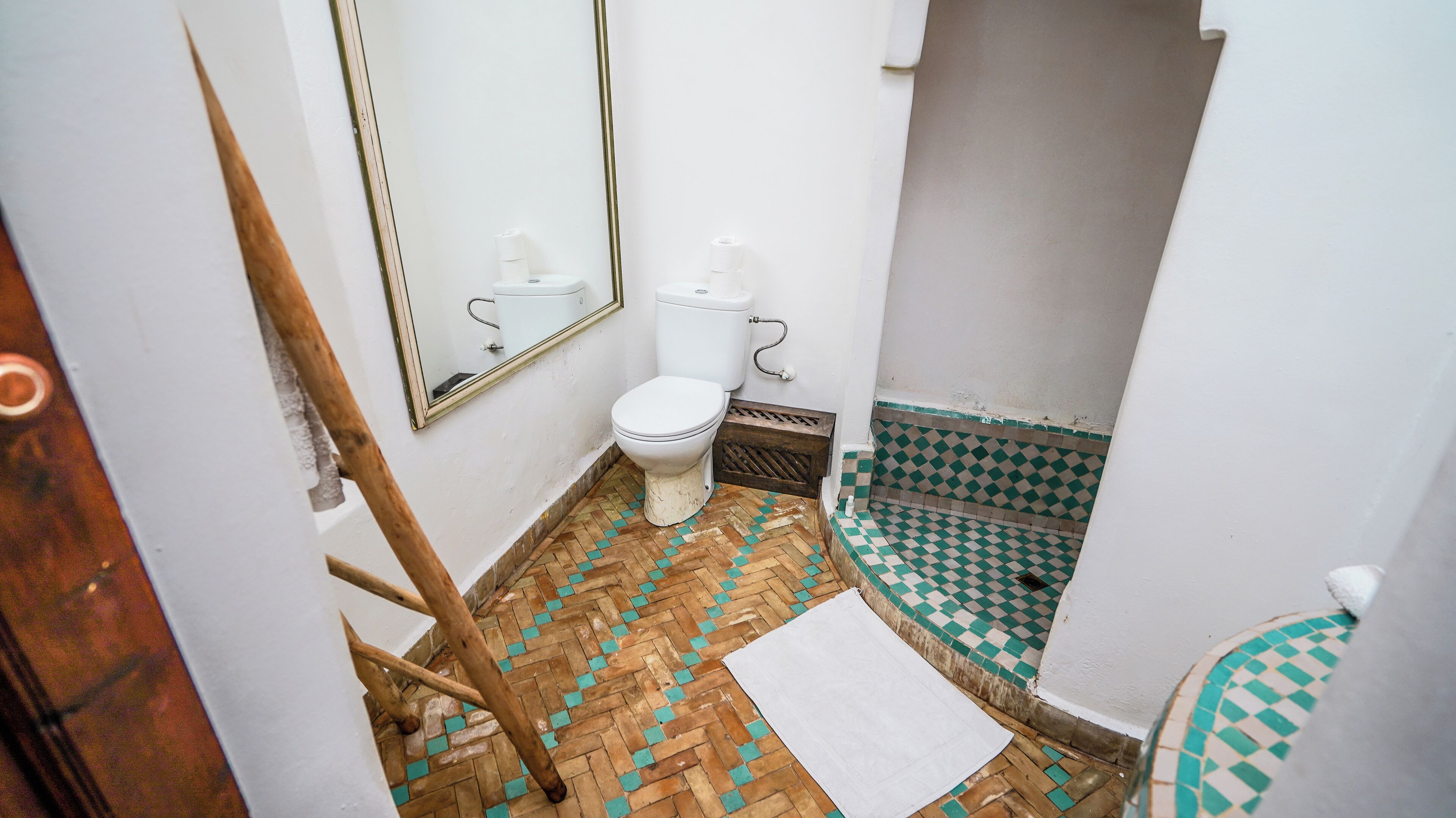 Un baño pequeño con inodoro, espejo y suelo con patrón de espiga.