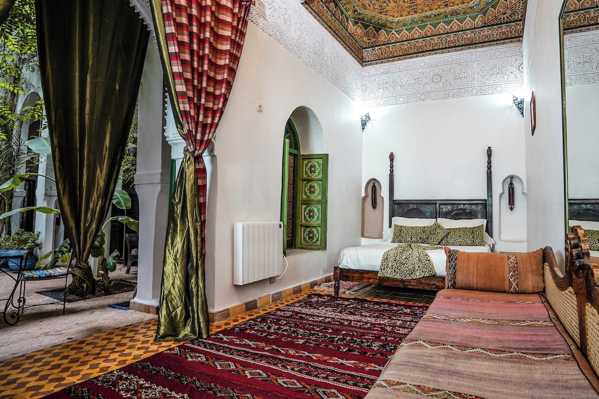 Une chambre traditionnelle avec un lit, un radiateur, une porte verte et des tapis à motifs.