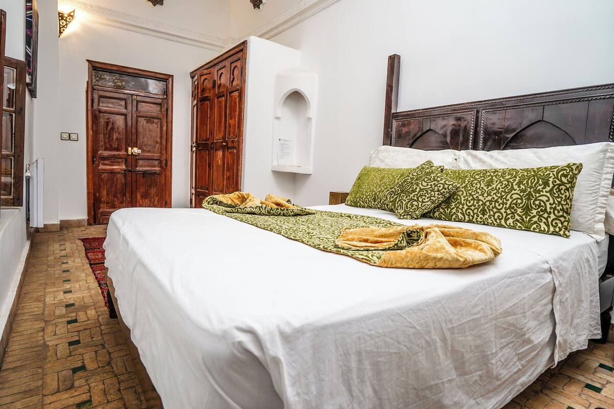 Une chambre avec un grand lit, une armoire en bois, un mur blanc et un tapis à motifs.