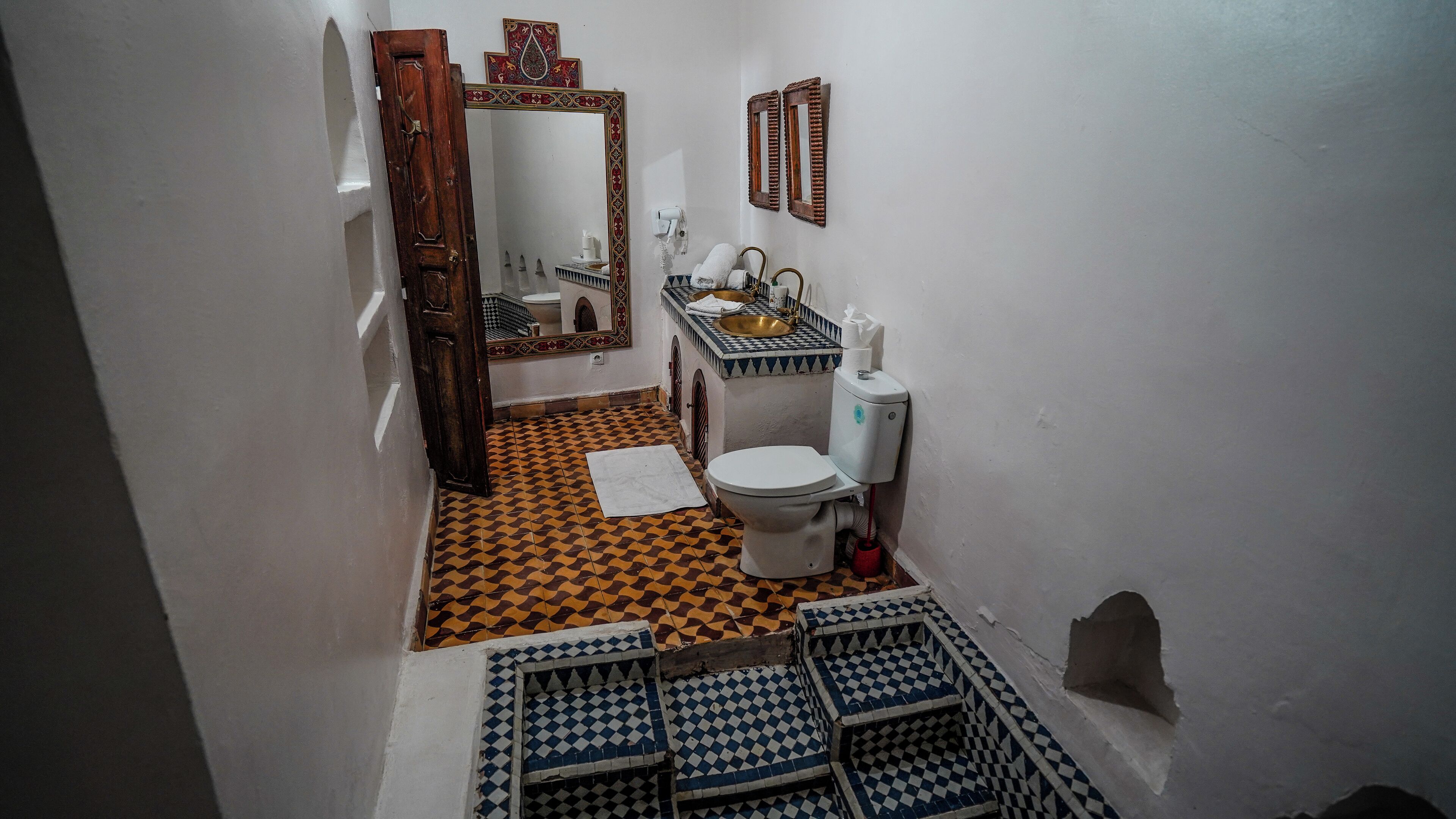 A narrow bathroom with a checkered floor, a toilet, a sink, a mirror, and a door.