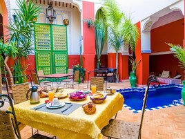 A dining area with a table set for breakfast, a pool, and a green wall with a bulletin board.